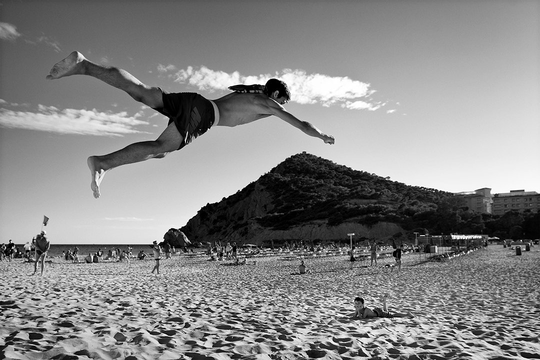 A person leaps into the air above a sandy beach.